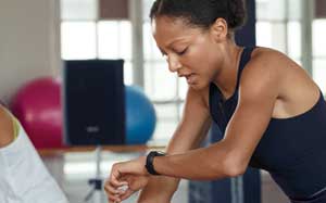Image of a girl on an exercise bike checking her Fitbit Versa smartwatch.