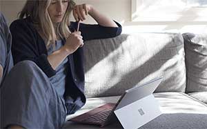 Image of a woman sitting on a sofa with a Surface Pro open on the table infront of her.