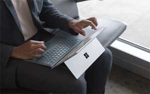 Image of a man sitting in a seat next to a window with a Microsoft Surface in his lap.