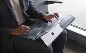 Image of a man sitting in a seat next to a window with a Microsoft Surface in his lap.