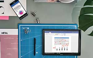 Image of a tablet and a mobile phone on a desk with office supplies around them.
