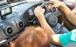 Image of the front 2 seats in a car with someone in the drivers and passenger seat and a TomTom sat nav mounted on the dashboard.