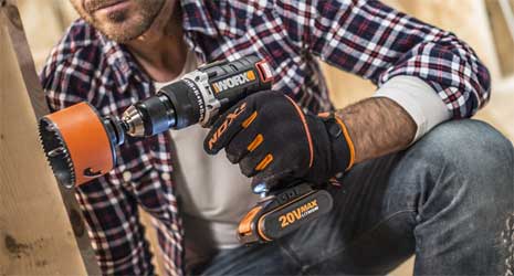 Image of a man kneeling down drilling into a wooden upright.