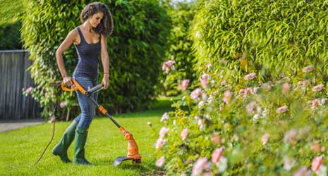 Image of a woman using a WORX grass trimmer in a landscaped garden.