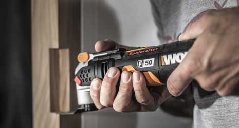 Image of a person using a WORX Sonicrafter multi-tool to clean up a piece of wood that has had an area cut out of it.