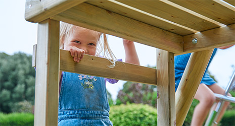 Image of a young child hanging by their arms from a TP climbing frame outside.