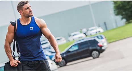 Image of a man dressed in gym wear and a sports bag on his shoulder walking outside near a road.