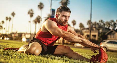Image of a man sitting on the grass stretching his leg mussles.